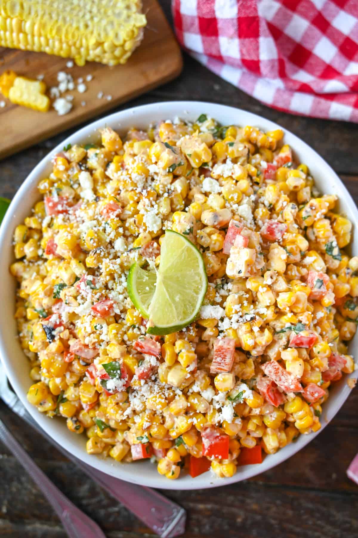 Sweet corn salad in a large whits bowl with corn on the conb on the side.