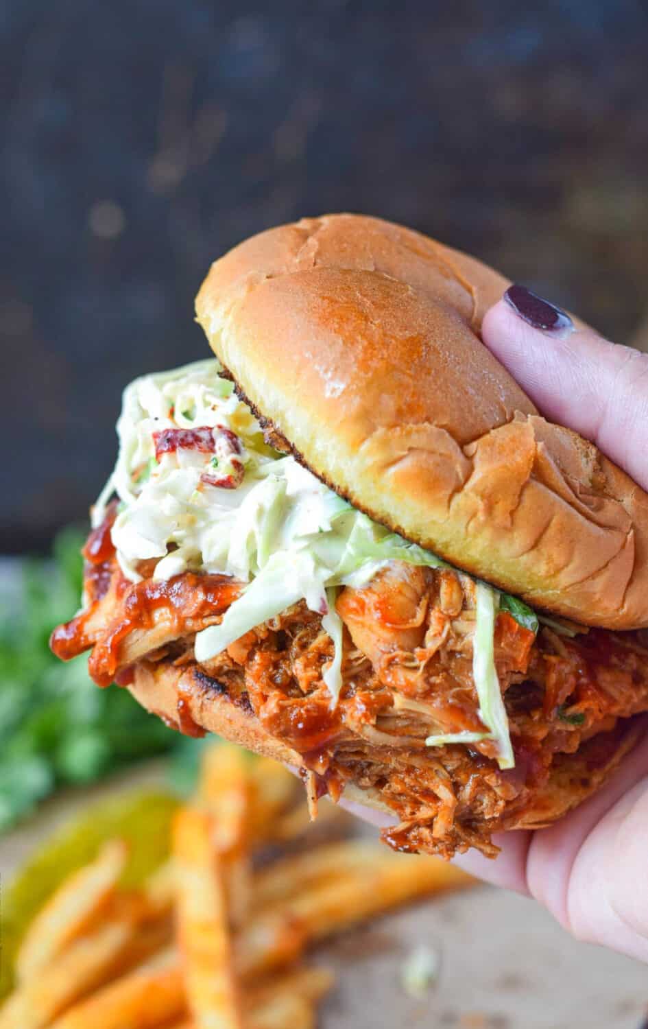 A chicken sandwich with coleslaw being held.
