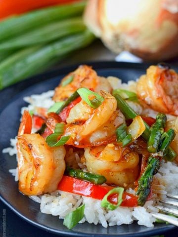 sweet chili shrimp stir fry on a black plate with a fork