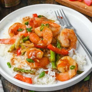 Sweet chili shrimp stir fry on top of coconut rice on a white plate.
