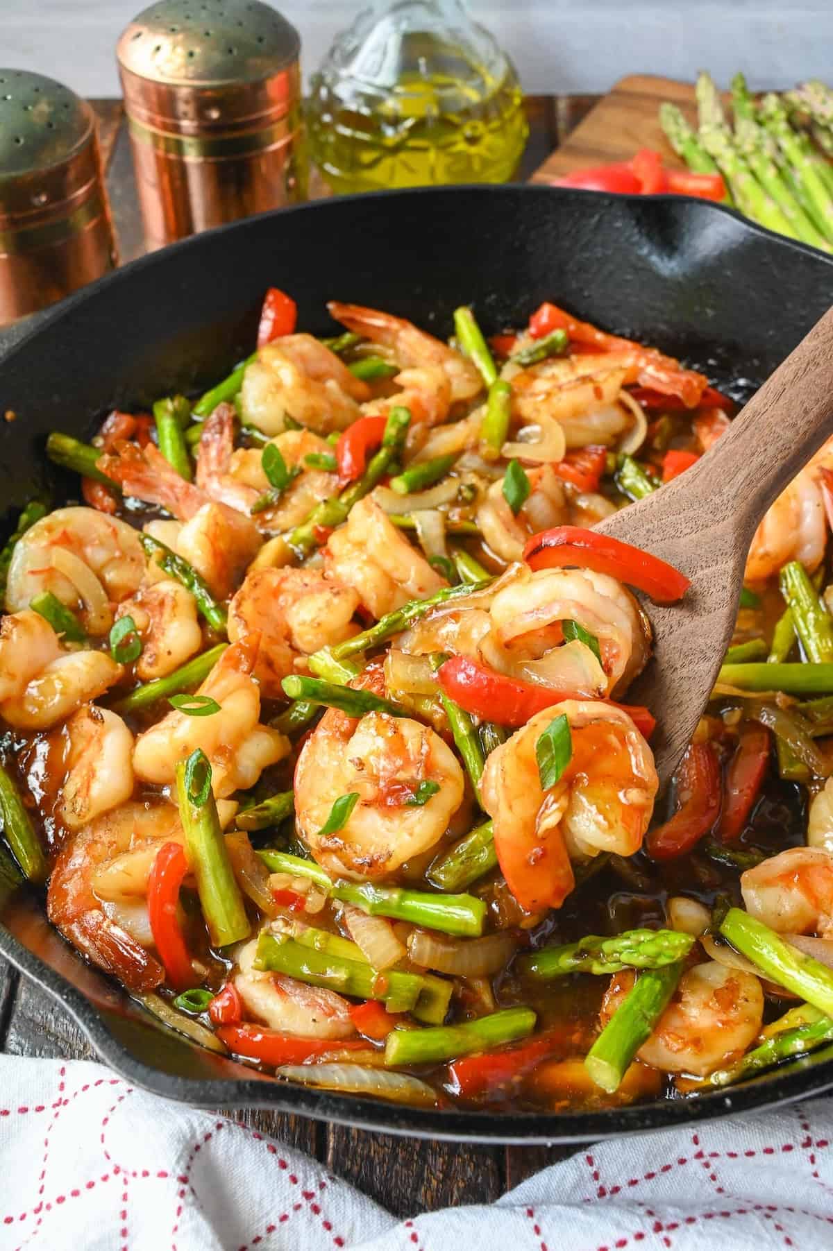Shrimp stir fry in a skillet and a spatula scooping some out. 