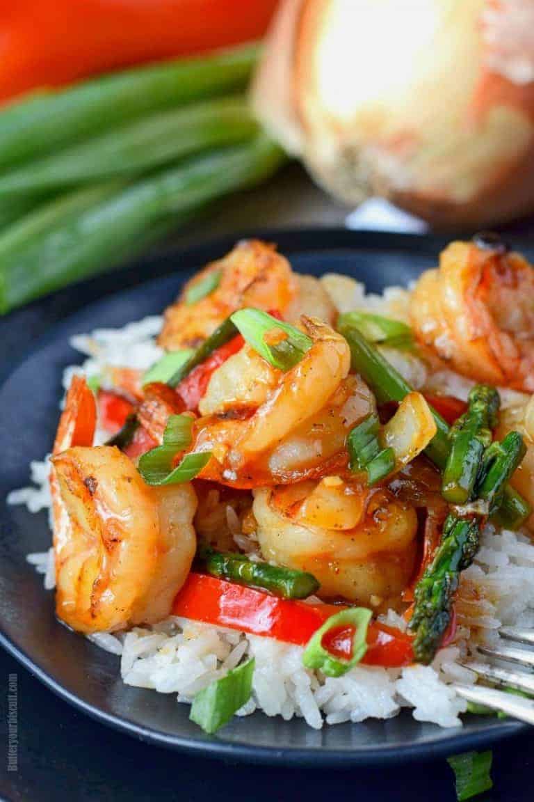 sweet chili shrimp stir fry on a black plate with a fork