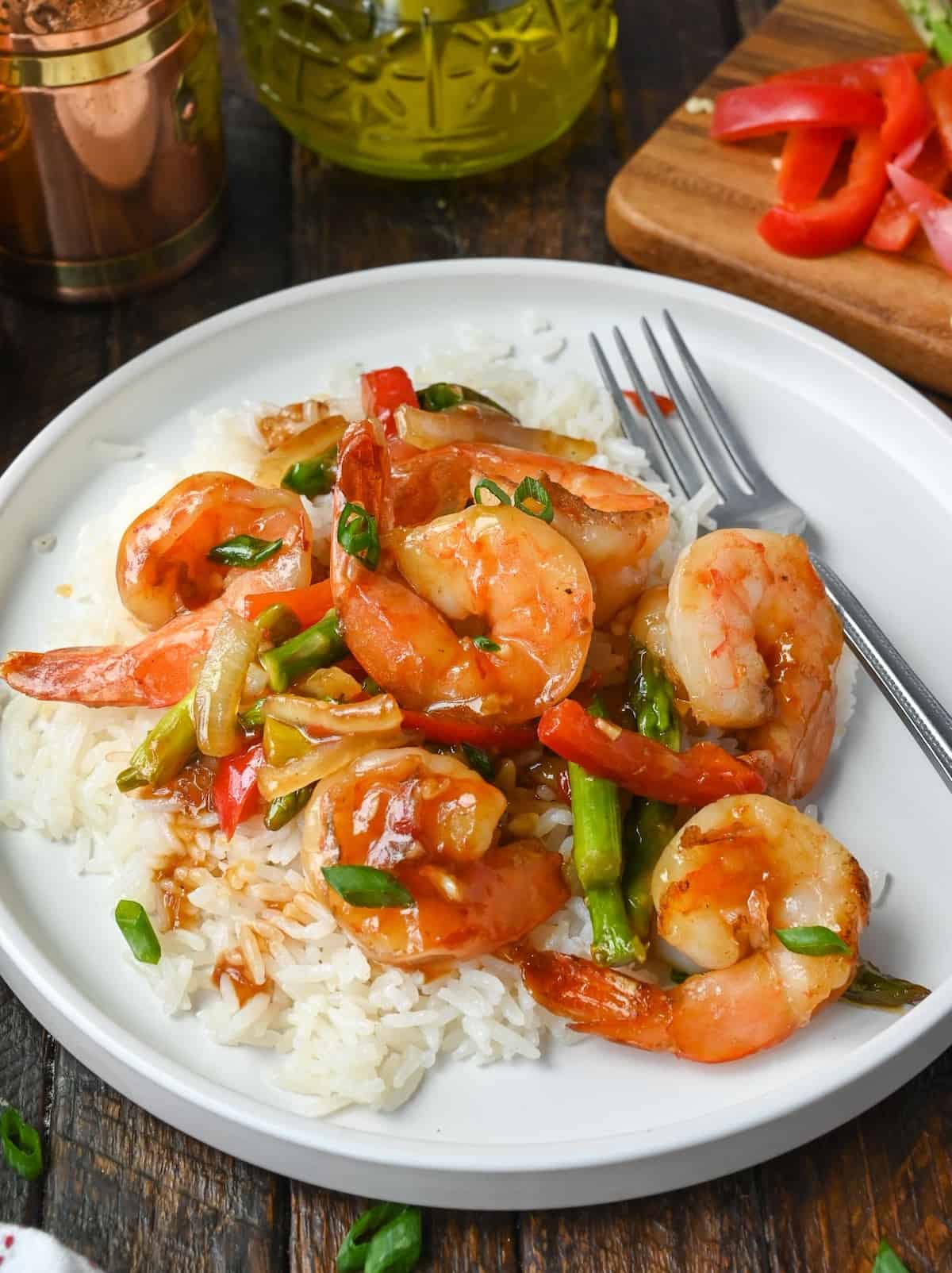 Sweet chili shrimp stir fry on top of coconut rice on a white plate.