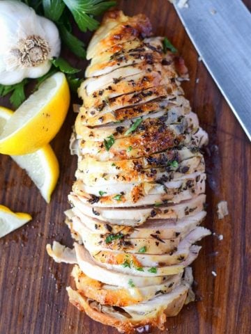 Brined herb chicken breasts on a cutting board with lemons and a fork