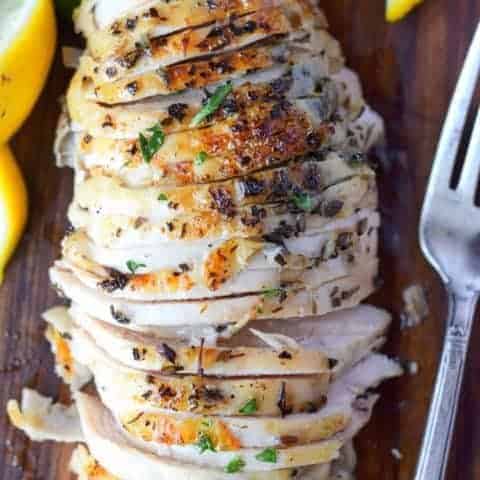Brined herb chicken breasts on a cutting board with lemons and a fork