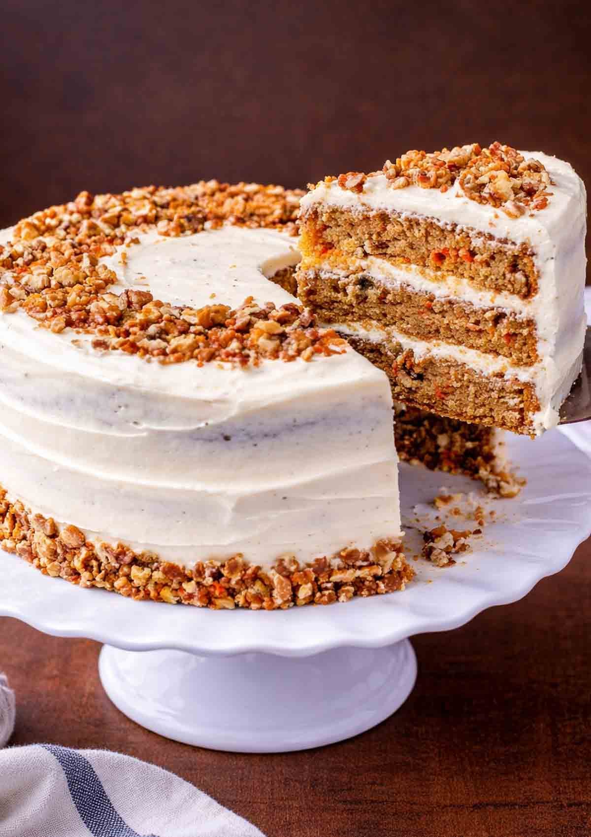 Carrot cake on a platter with a slice removed.