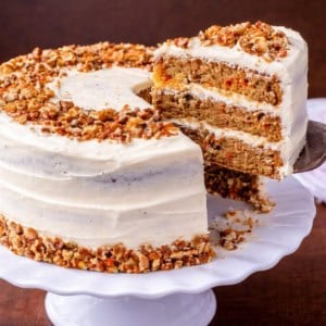 Carrot cake on a platter with a slice removed.
