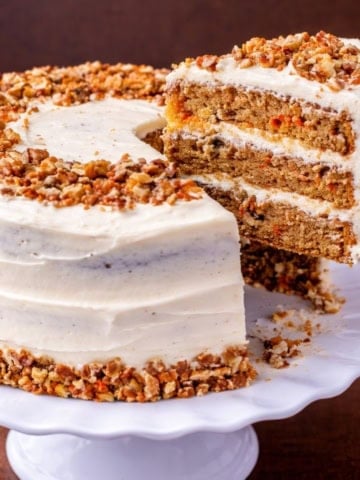 Carrot cake on a platter with a slice removed.