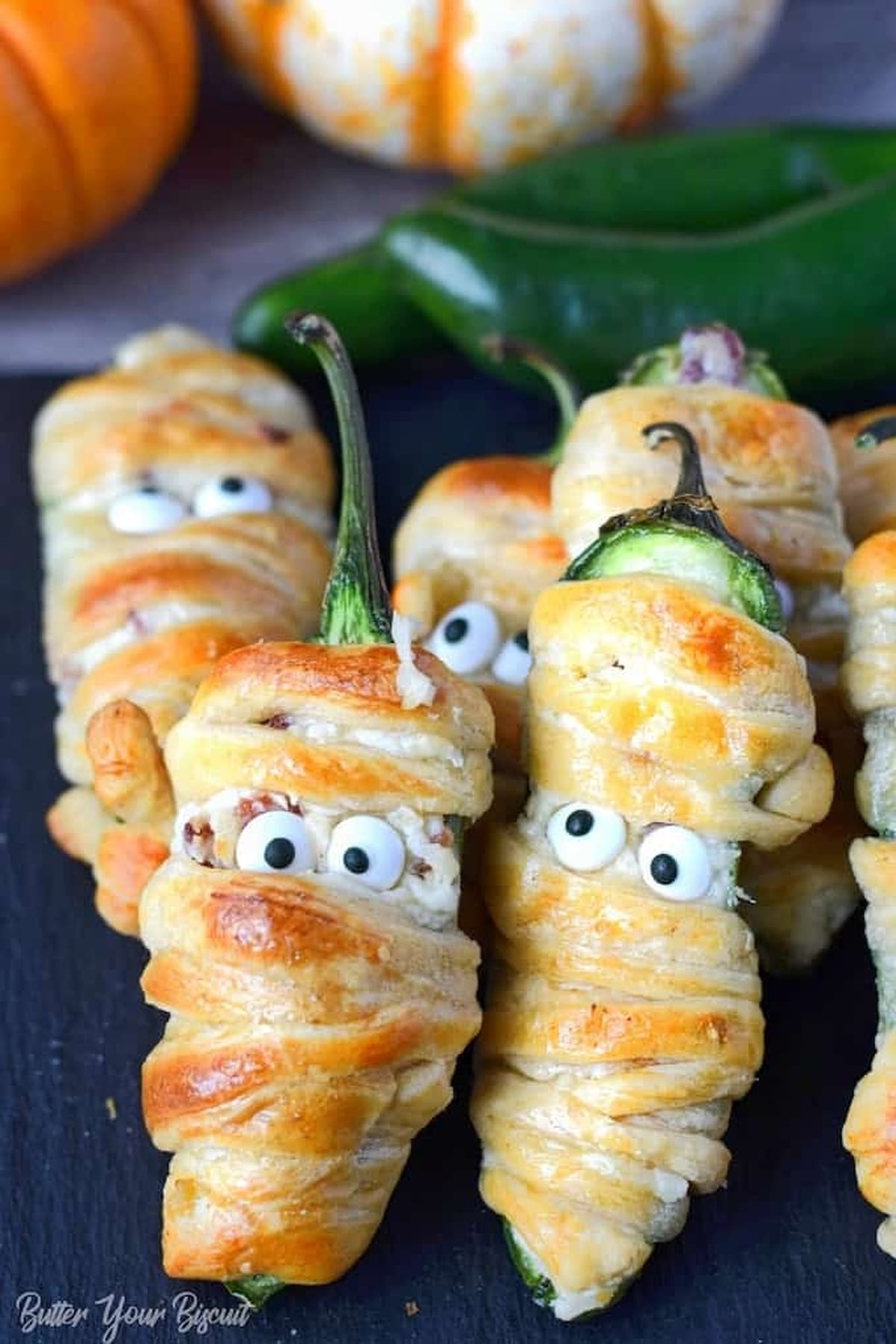 Bacon jalapeno crescent roll wrapped mummies on a cutting board.