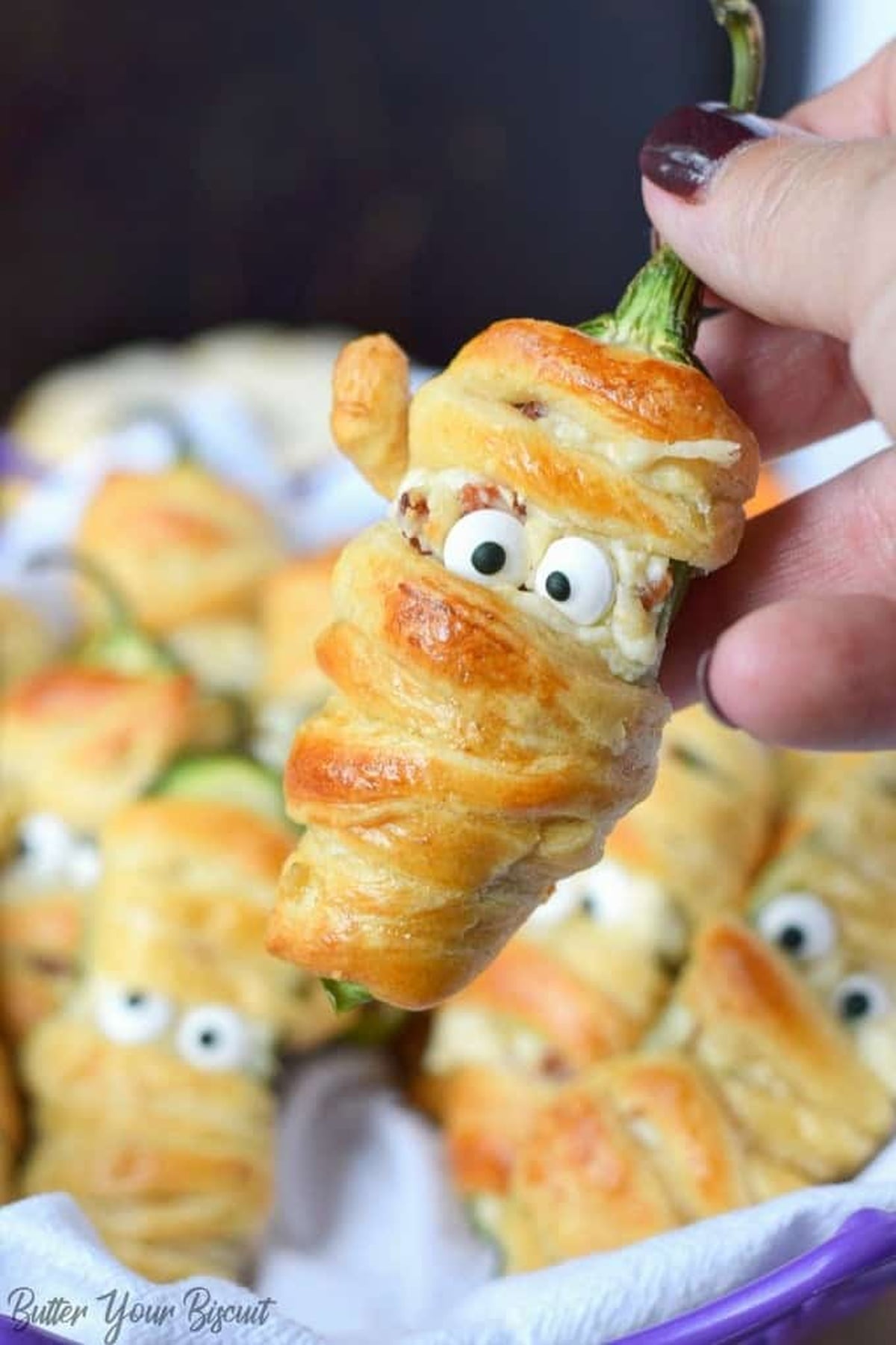 A bacon jalapeno mummy wrapped in crescent roll dough being held.
