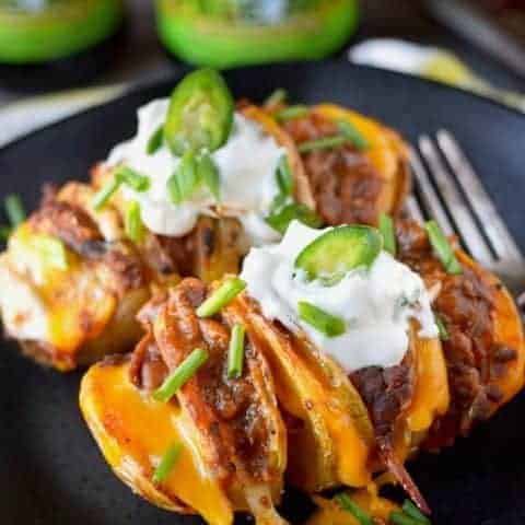 Two chili cheese hasselback potatoes on a black plate topped with sour cream
