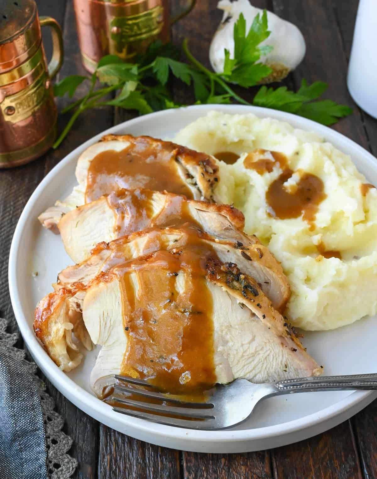 Turkey gravy poured on top of turkey on a white plate with mashed potatoes.