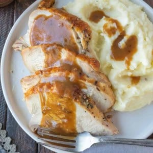 Turkey gravy poured on top of turkey on a white plate with mashed potatoes.