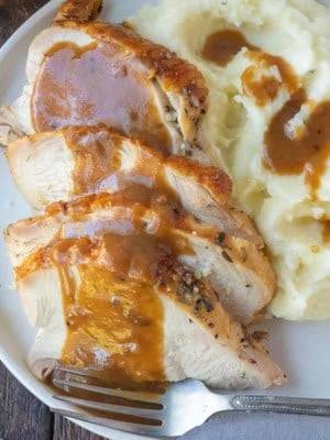 Turkey gravy poured on top of turkey on a white plate with mashed potatoes.