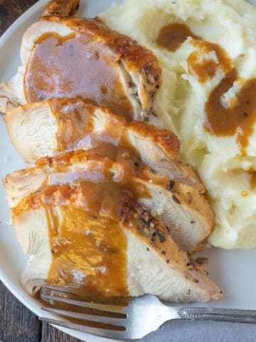 Turkey gravy poured on top of turkey on a white plate with mashed potatoes.