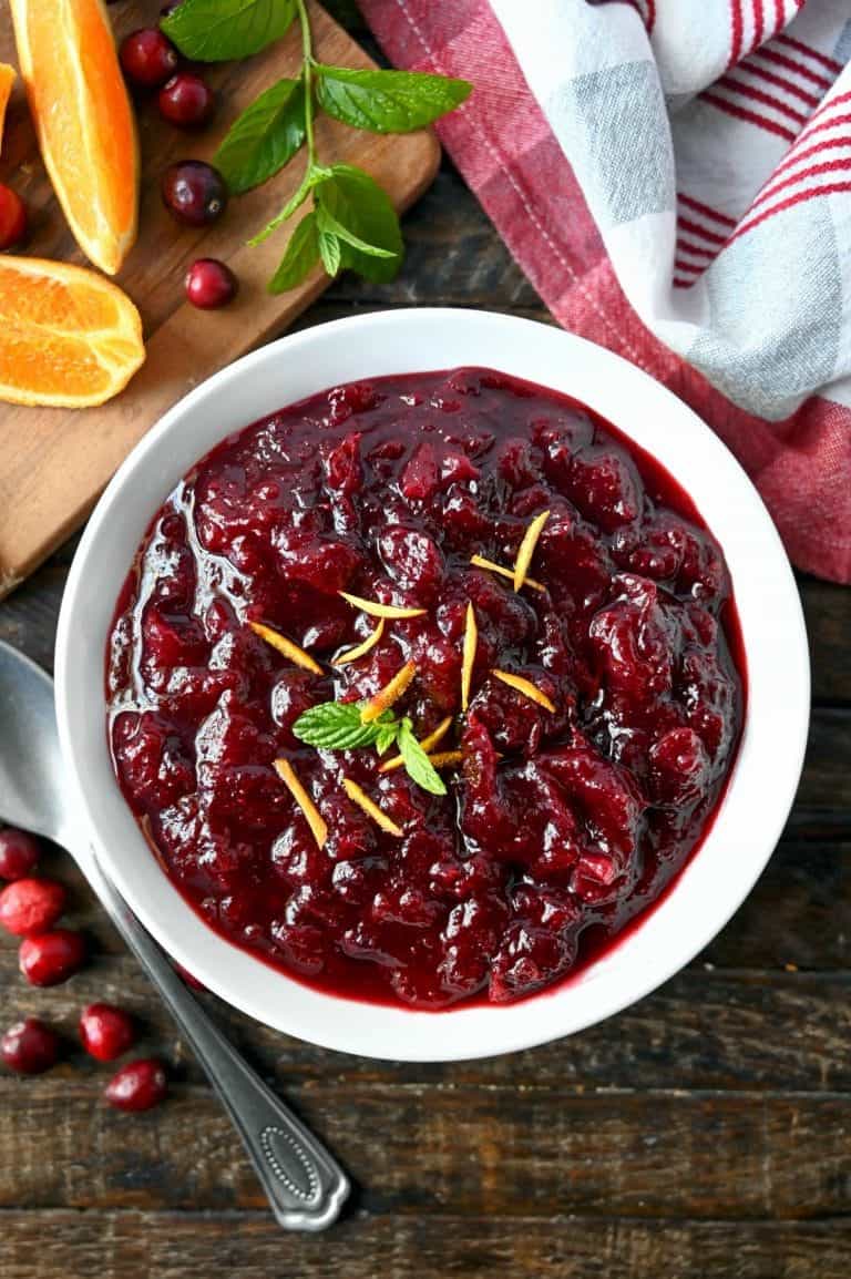 Homemade cranberry sauce in a white bowl with orange peel shavings on top and a sprig of mint.