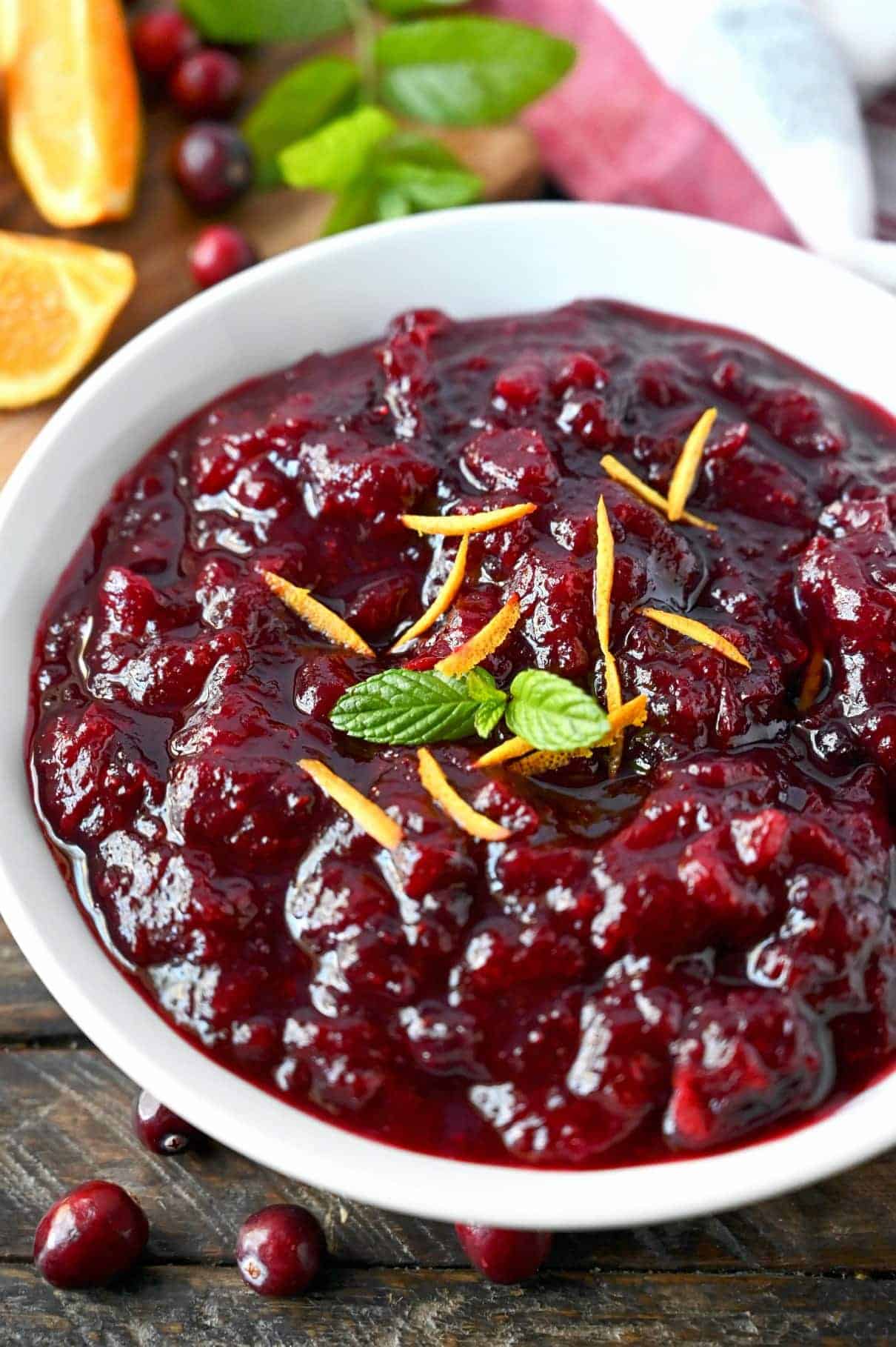 A bowl of homemade cranberry sauce, with a sprig of mint and orange peel shavings on top.