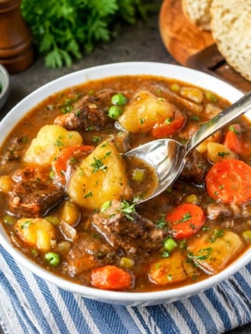 A bowl of hearty beef stew with a spoon scooping up a bite.
