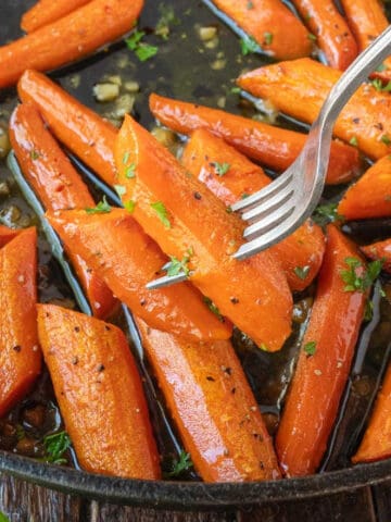 Garlic roasted carrots being in a pan and a fork picking up two.