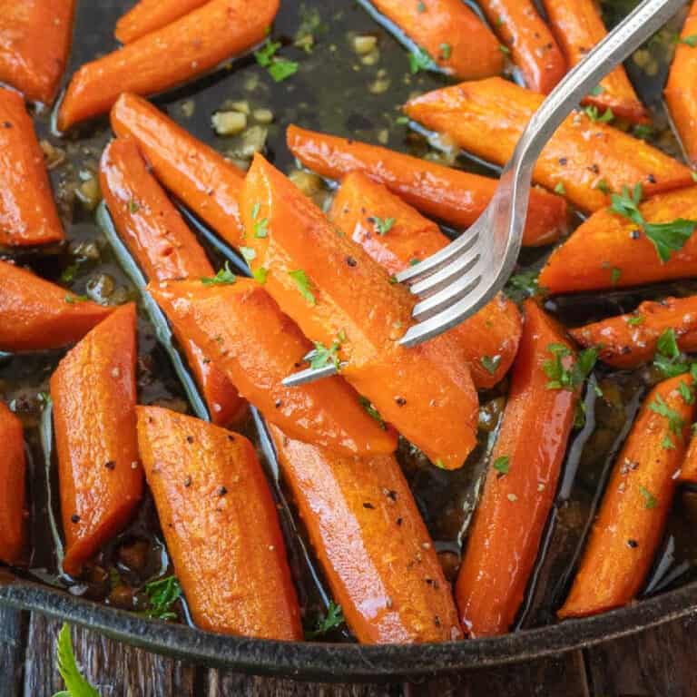 Garlic roasted carrots being in a pan and a fork picking up two.
