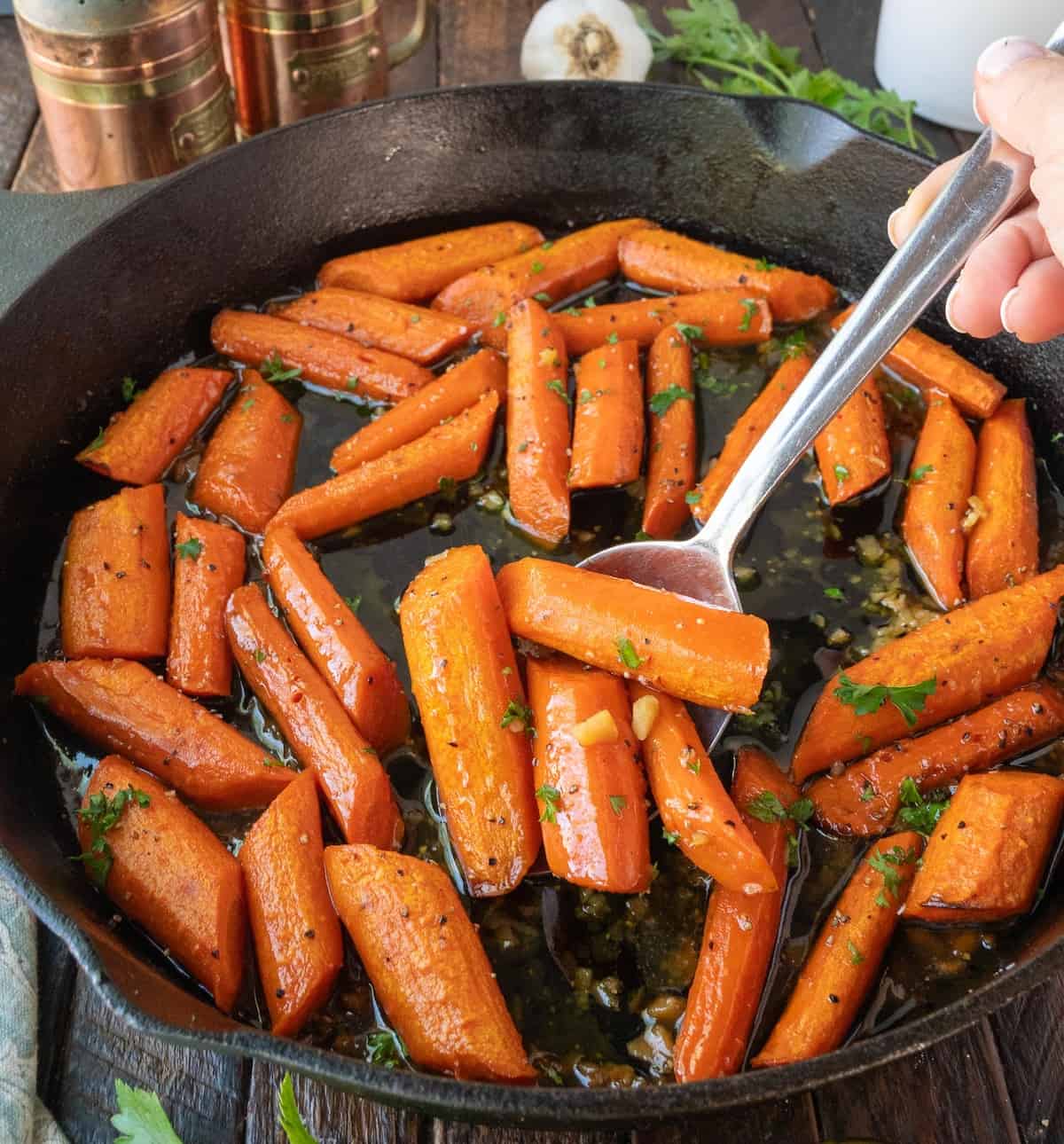 Roasted carrots in a cast iron pan and a spoon scooping out a few.