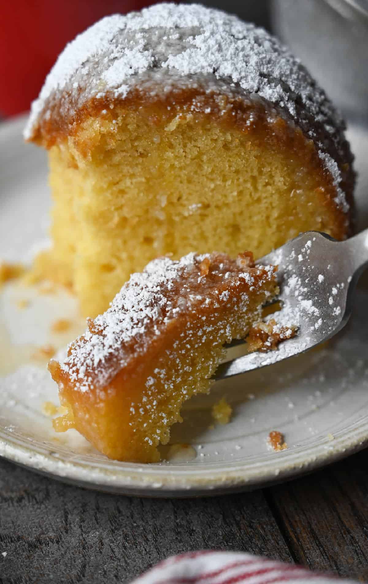 A piece of rum cake on a plate with a bit taken off.