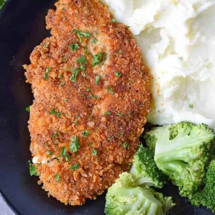 crispy chicken cutlets on a black plate with mashed potatoes and broccoli