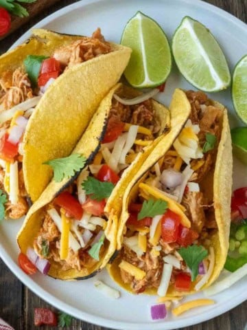 Three salsa chicken tacos with some sliced limes.