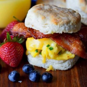 bacon egg and cheese biscuit sandwich on a cutting board with blueberries and strawberries and orange juice