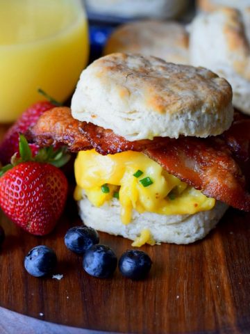 bacon egg and cheese biscuit sandwich on a cutting board with blueberries and strawberries and orange juice