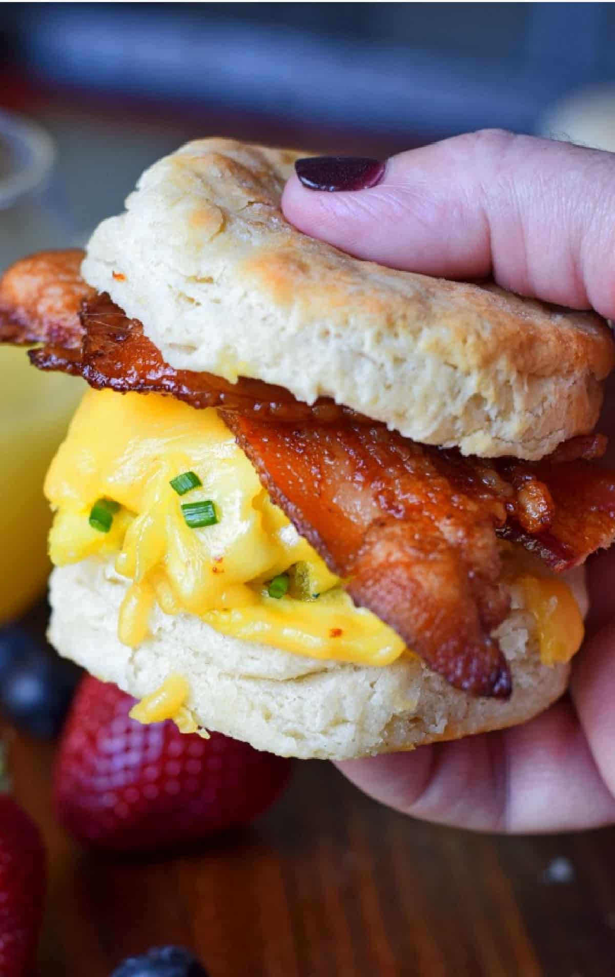 Bacon egg and cheese biscuit being held in a hand.
