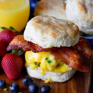 A biscuit sandwich on a cutting board with strawberries and orange juice.