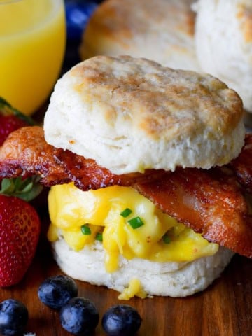 A biscuit sandwich on a cutting board with strawberries and orange juice.