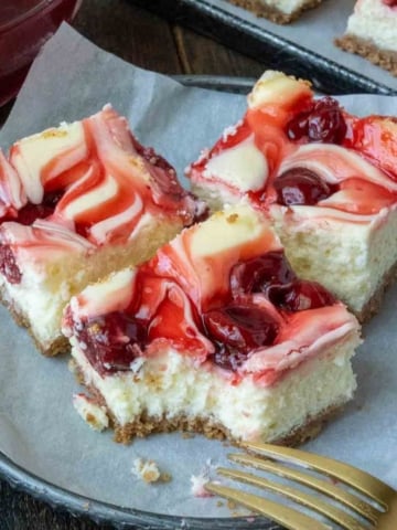 Three cherry cheesecake bars on a plate with a fork.