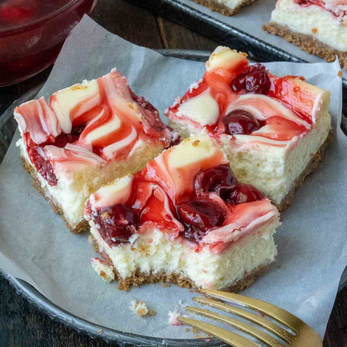 Three cherry cheesecake bars on a plate with a fork.