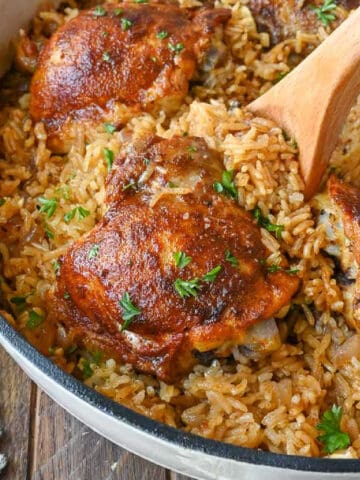 A wooden spoon scooping of some rice and a piece of chicken.