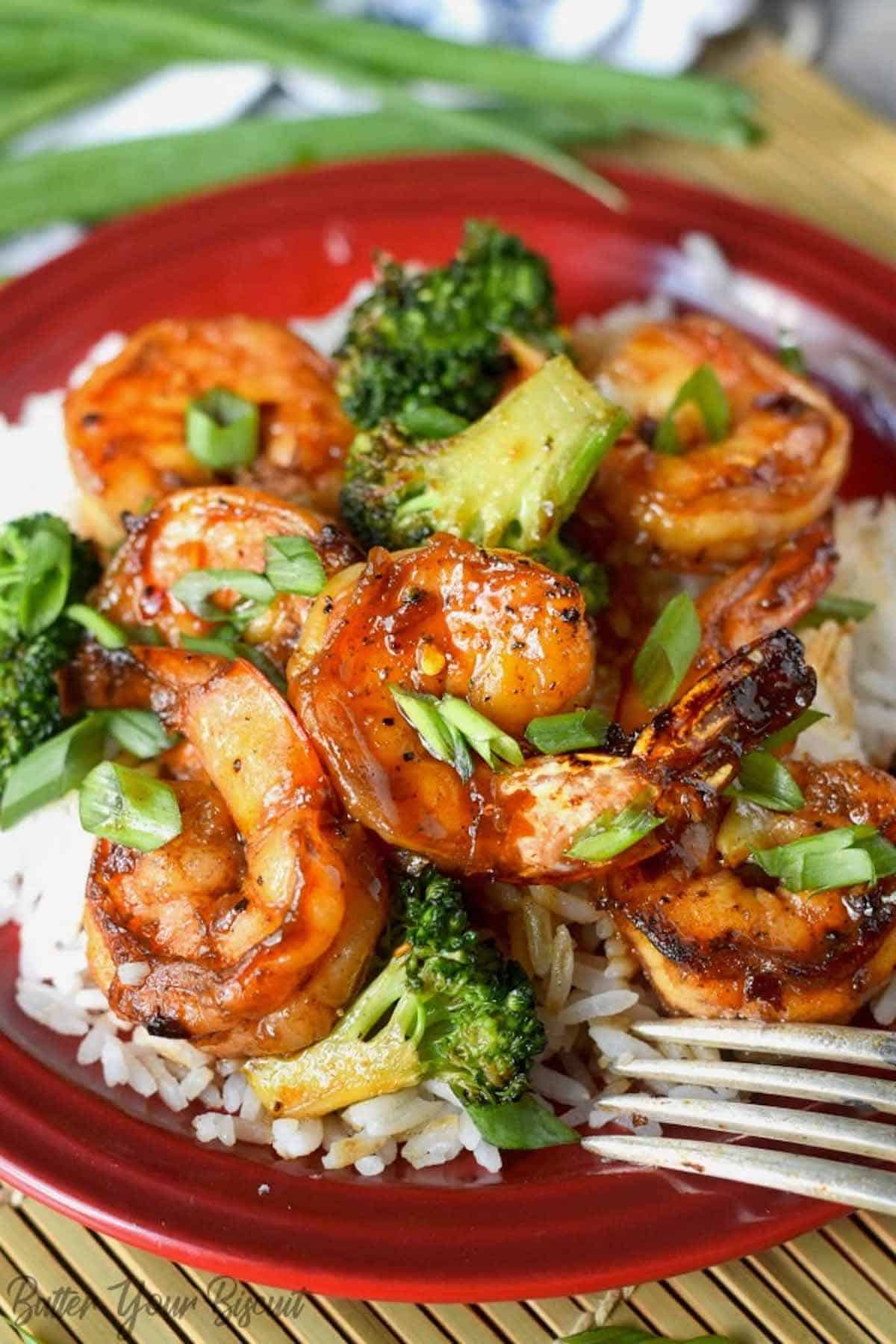 A plate of white rice with honey garlic shrimp and broccoli on top.