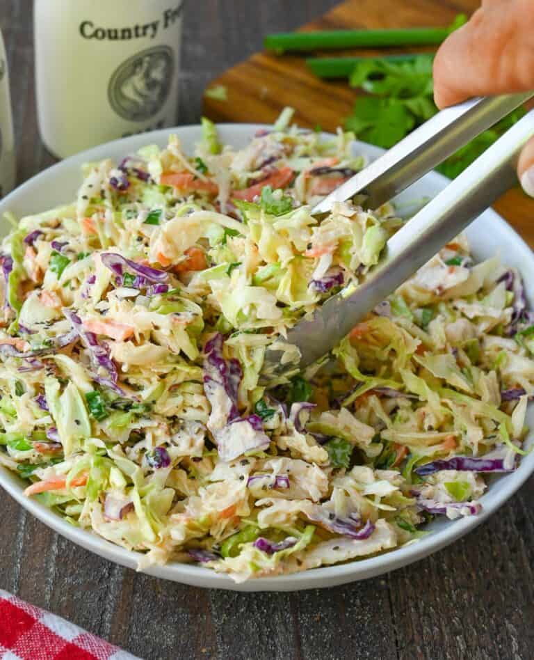 Tongs picking up a serving of coleslaw.