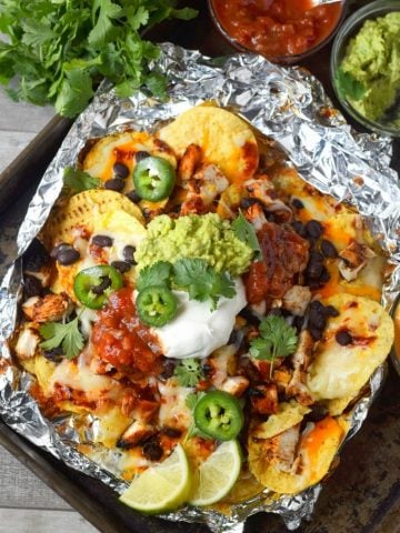 foil packet chicken nachos on a baking sheet with a side of salsa and guacamole