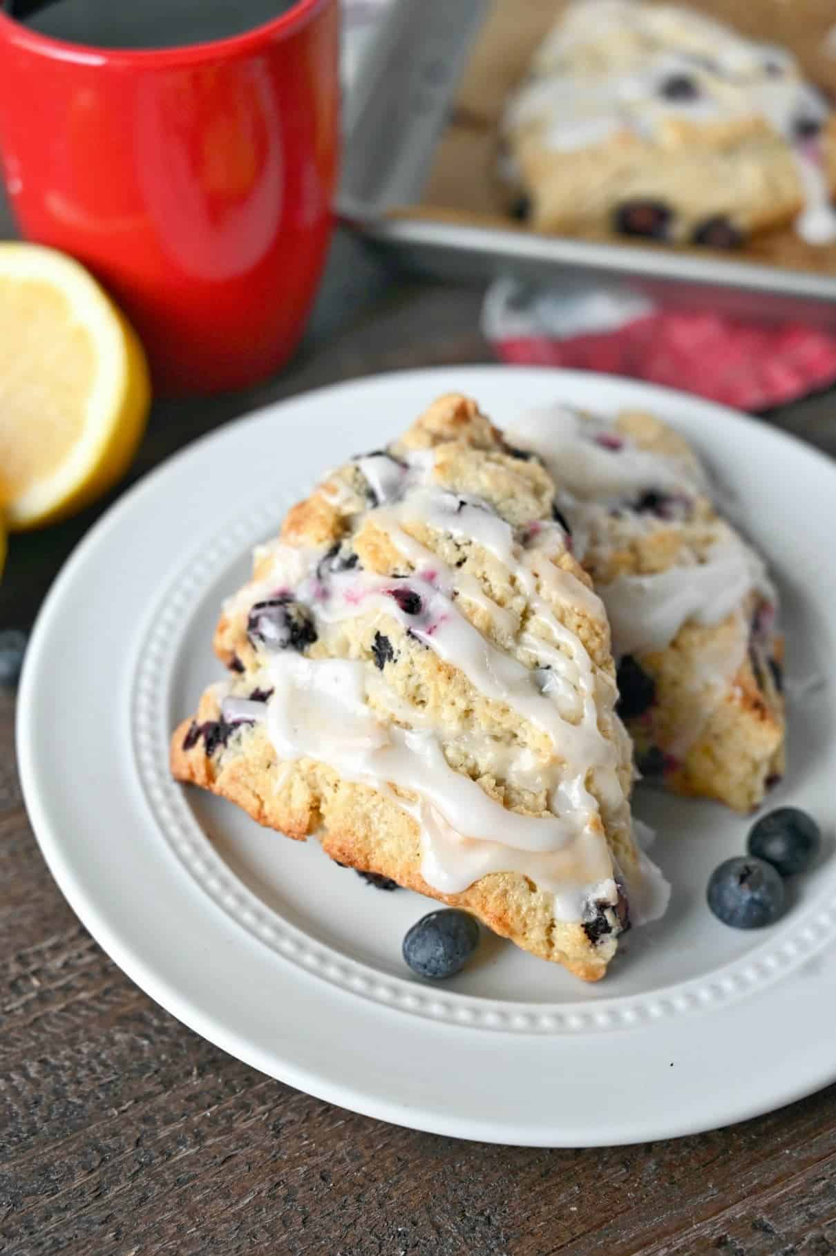 Lemon blueberry scone on a white plate with a red cup of coffee.