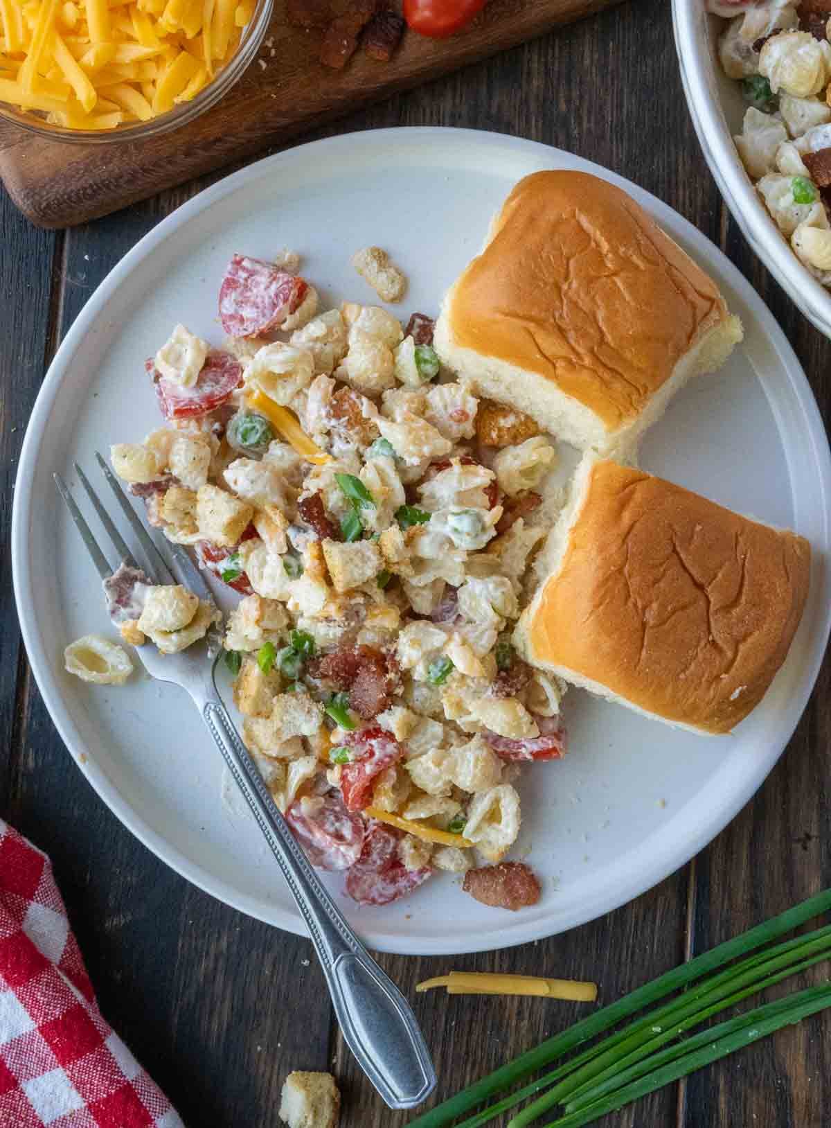 Pasta salad on a white plate with dinner rolls.