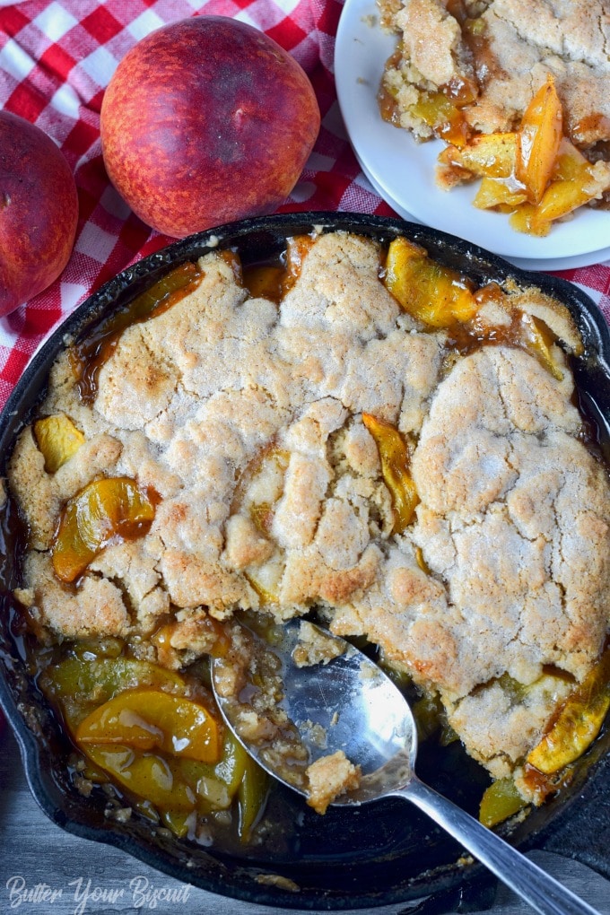 Pech cobbler in a cast iron skillet with a metal spoon that has removed a scoop.
