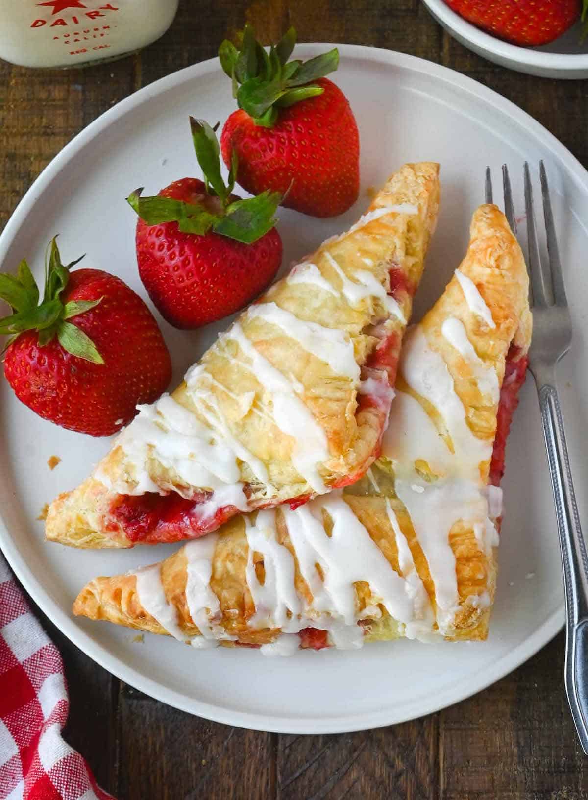 Two strawberry turnovers on a white plate with a few fresh strawberries.