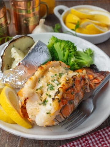 Broiled lobster tail on a plate with a potato and broccoli.