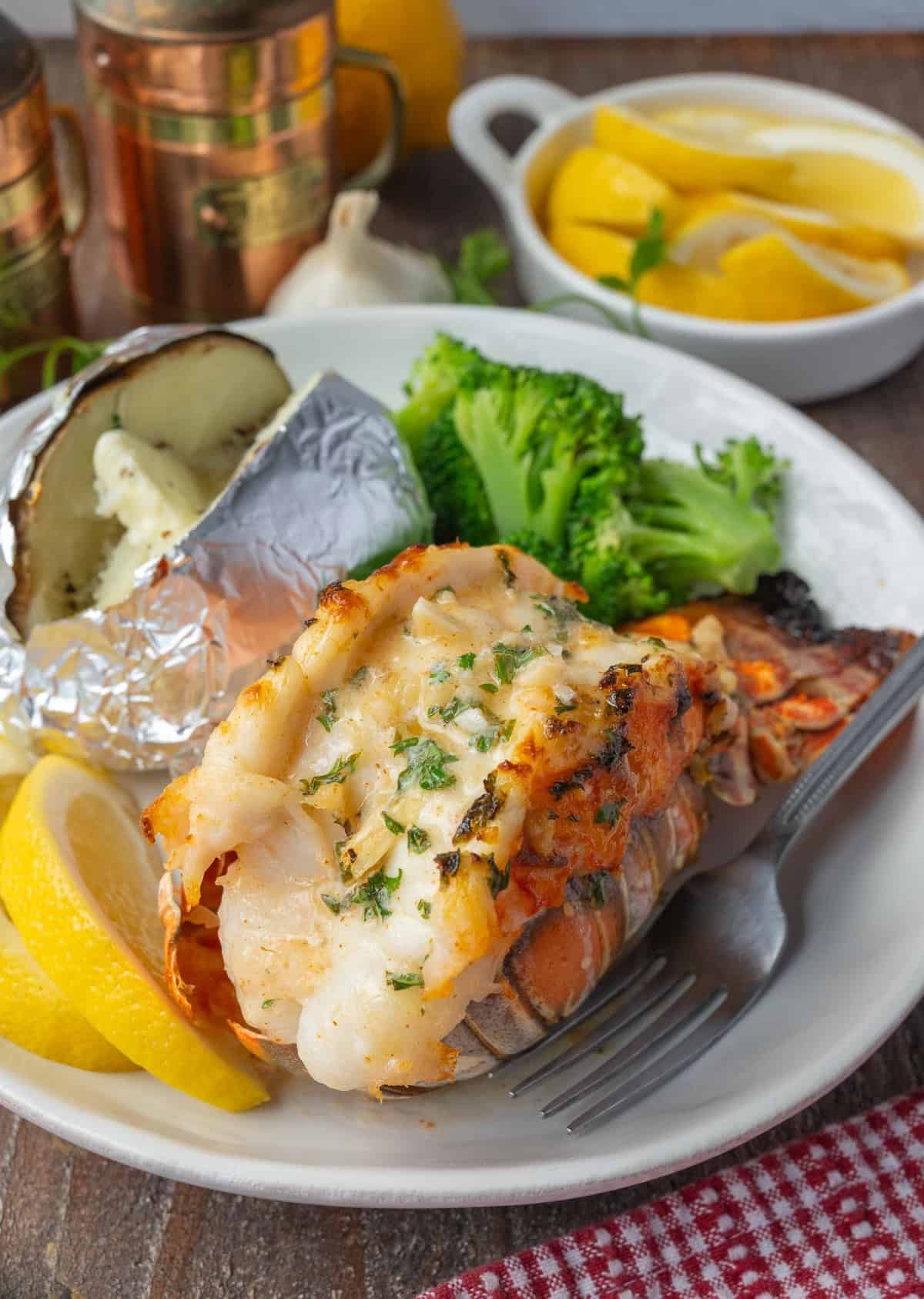 Broiled lobster tail on a plate with a potato and broccoli.