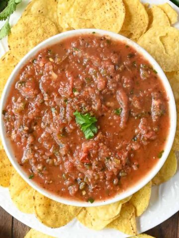 Salsa in a white bowl with tortilla chips all around.