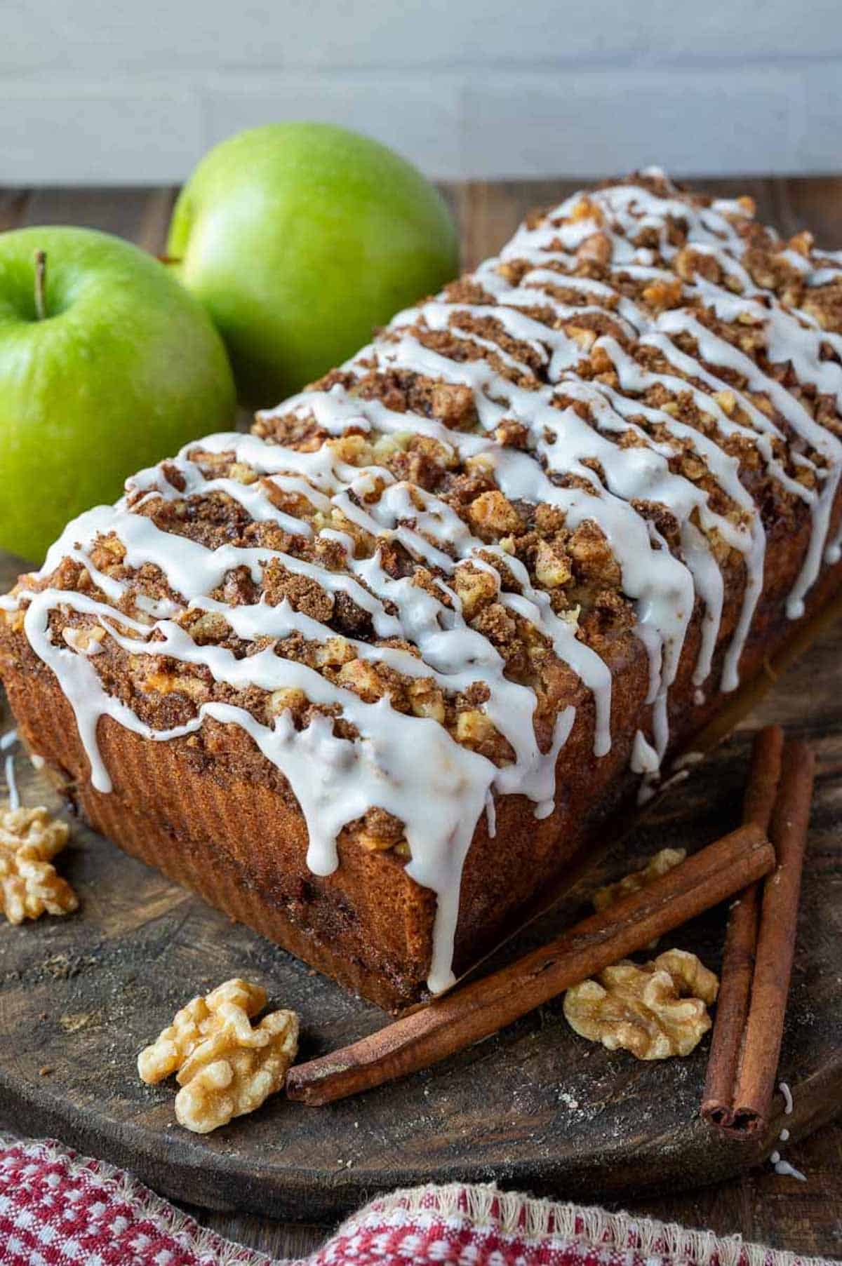 Apple fritter walnut bread on a cutting board with walnuts and apples.
