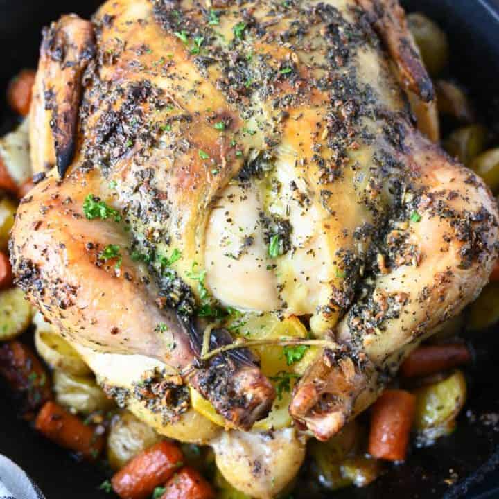 A whole lemon garlic roasted chicken on top of roasted veggies in a cast iron skillet.