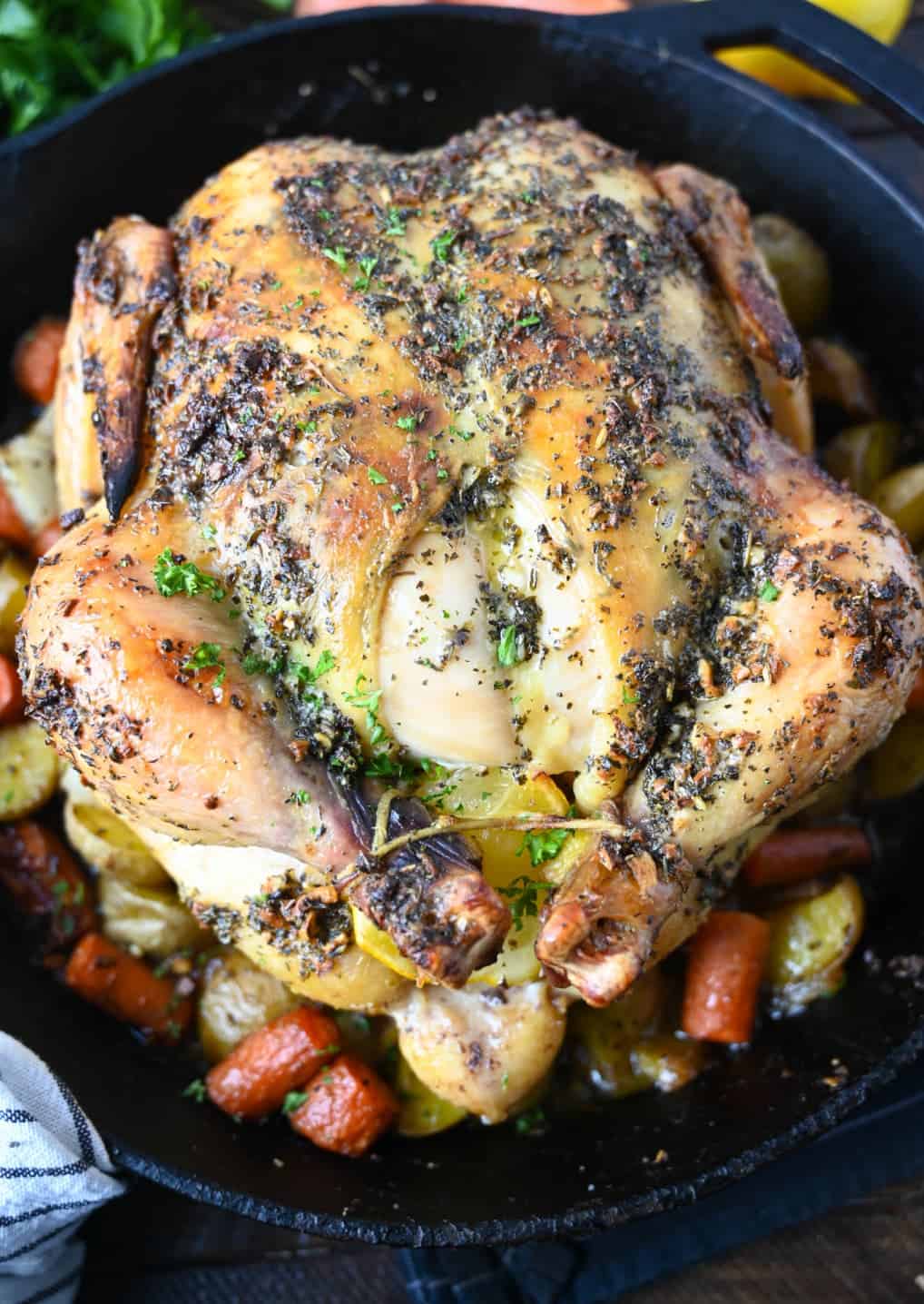 A whole lemon garlic roasted chicken on top of roasted veggies in a cast-iron skillet.