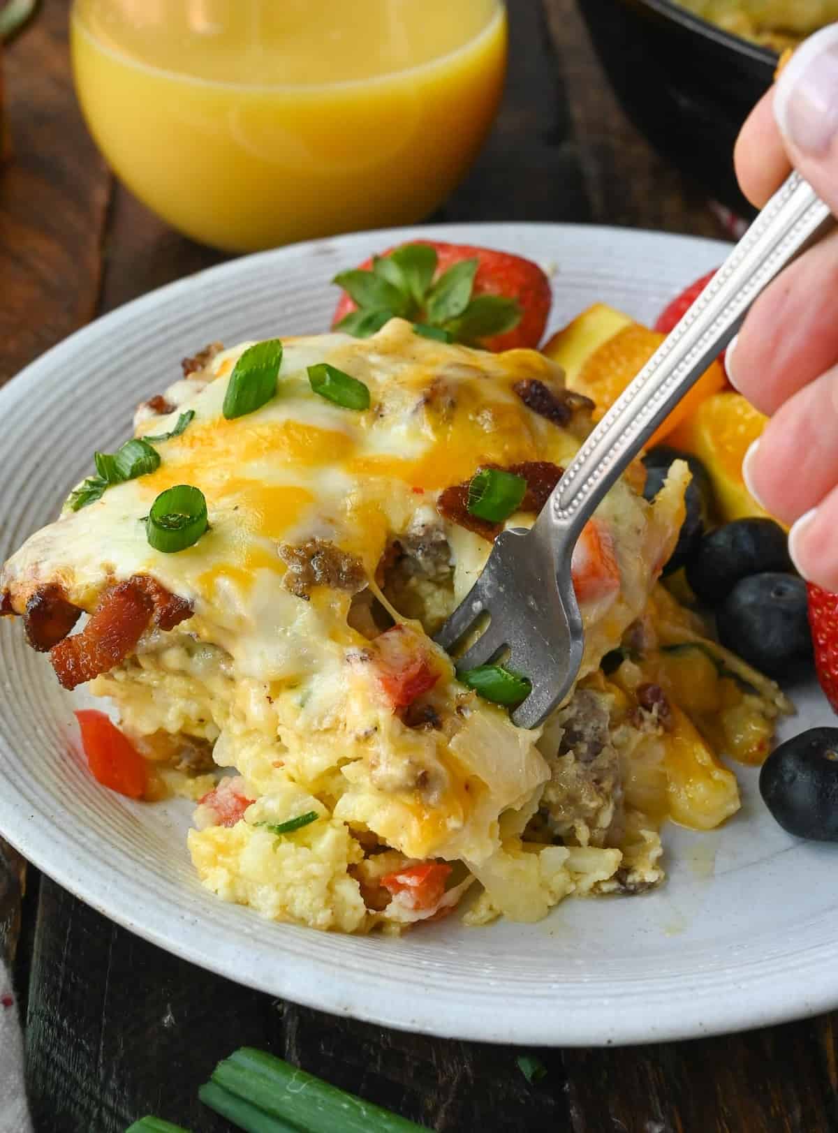 A fork picking up a bite of breakfast casserole on a plate.